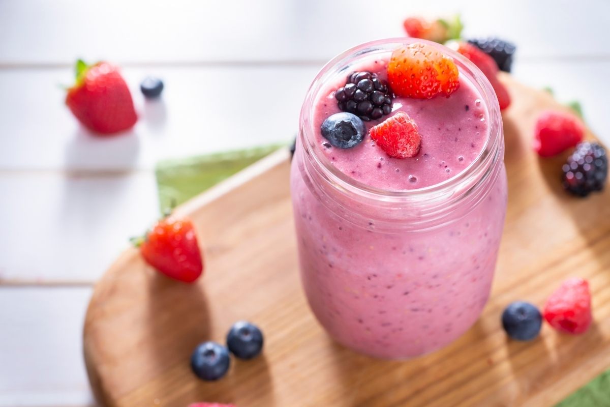 A container with berry shake surrounded with berries.