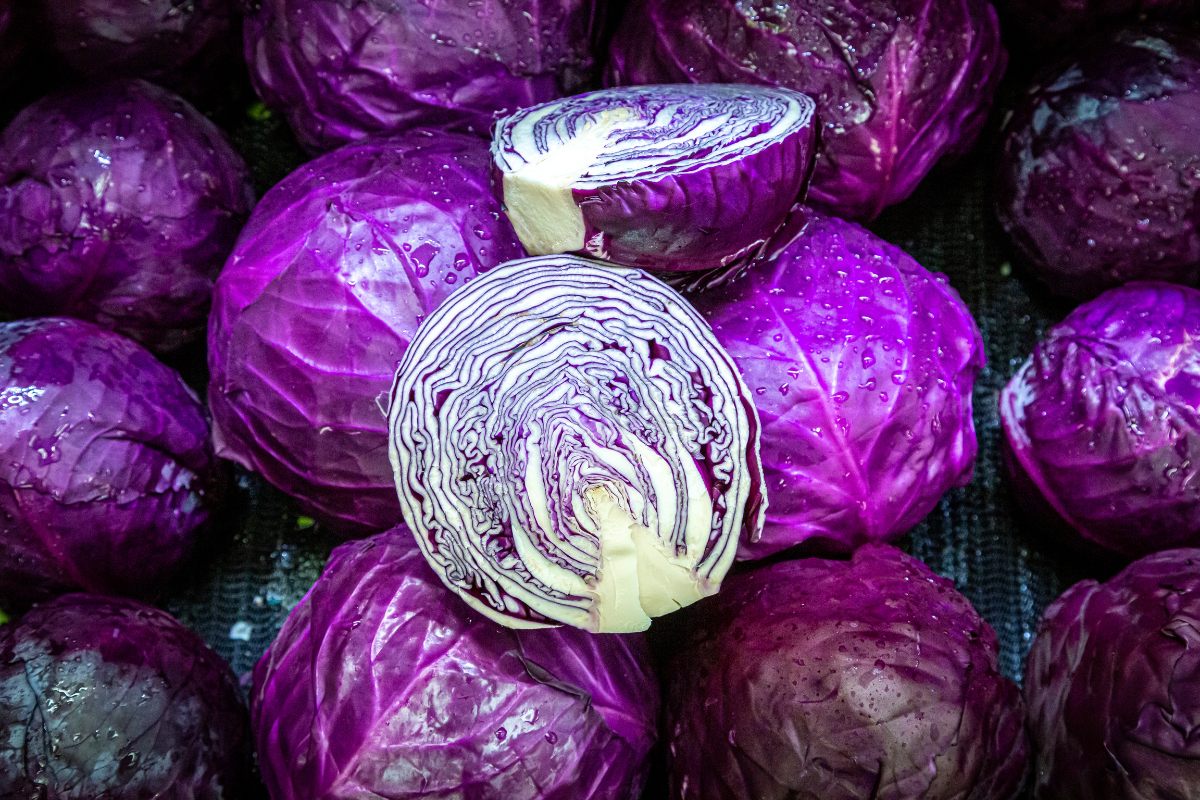 A pile of red cabbages with the one on top cut in half.