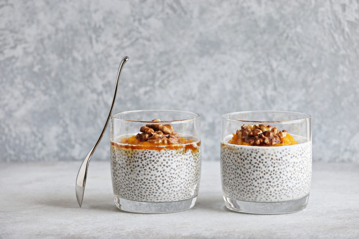 A glass with chia pudding decorated with pumpkin puree and nuts.