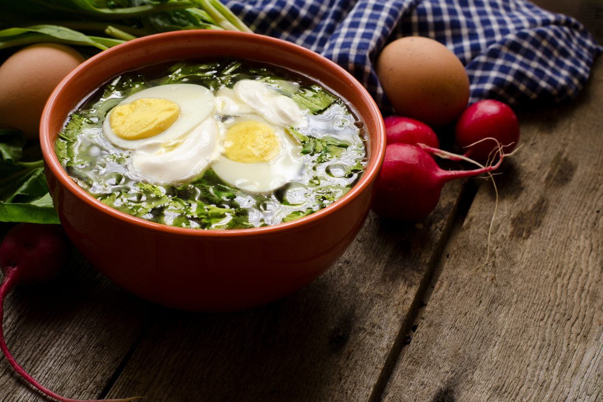 A bowl of sorrel soup served with boiled egg and sour cream.