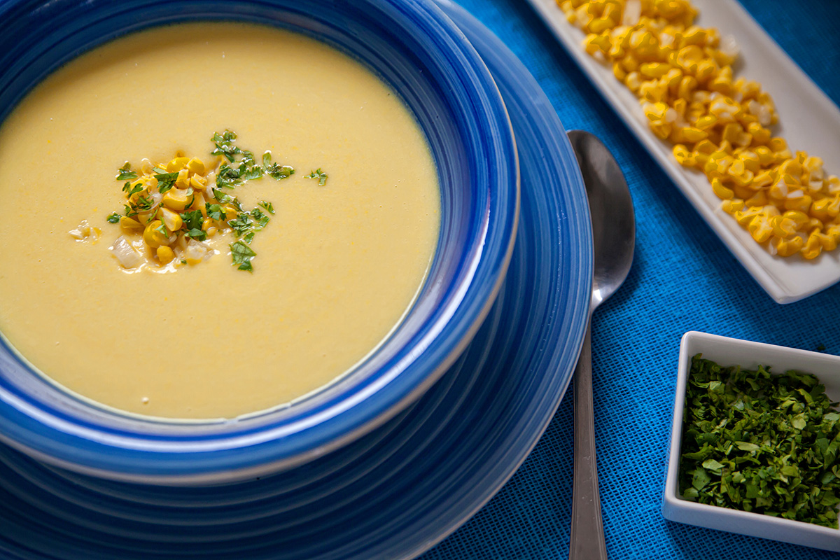 A bowl of corn soup decorated with chopped coriander and corn kernels.