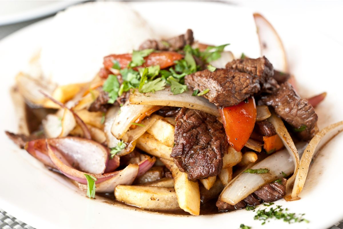A plate with sitr fried meat and vegetables with soy sauce and liquied known as Peruvian lomo saltado.