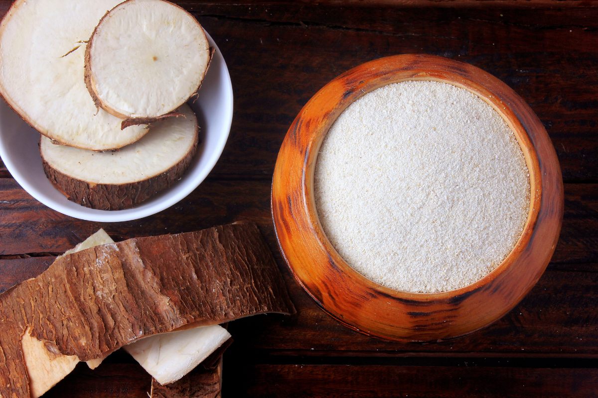 Cassava flour in a wooden bowl next to pieces of fresh cassava.