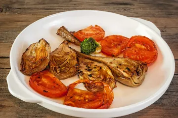 Alcachofas y tomate asados en un plato.