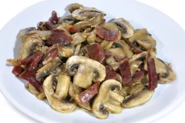 Un plato de champiñones salteados con jamón serrano.