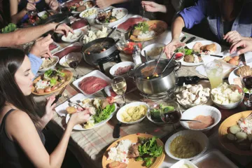 Un grupo de amigos compartiendo fondue sentados alrededor de una mesa.
