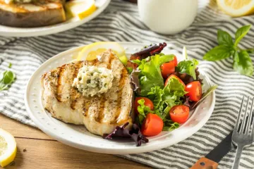 Un plato con pez espada a la parrilla acompañado de salsa y ensalada.