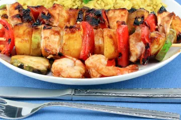 BRochetas de pollo y piña con su acompañamiento en un plato.