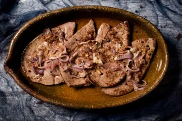 Cuatro filetes de hígado encebollado en una fuente de barro.