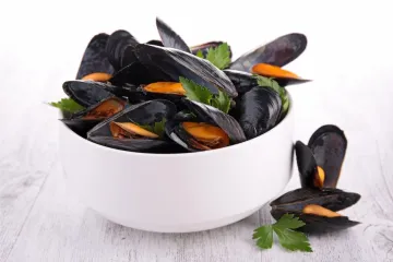 Un cuenco blanco con mejillones ya cocidos decorados con perejil.
