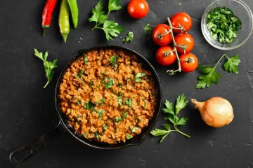 Curry kima en una sartén de hierro rodeado de algunos de sus ingredientes.