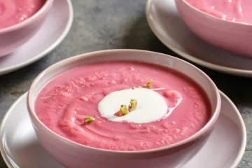 Un cuenco con sopa de terciopelo rosa decorada con crema de coco y pistacho picado.
