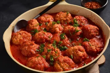 Una cazuela de cerámica con albóndigas de sepia y gambas en salsa de tomate.