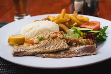 Atún a la parrilla servido con arroz, patatas fritas y ensalada.