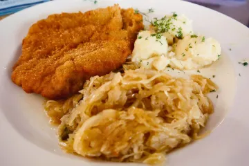 Un plato con un filete de cerdo empanado acompañado con repollo encurtido y puré de patata, al estilo polaco.