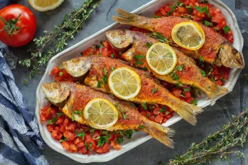 Salmonetes al horno servidos sobre una cama de tomate concasé y decorados con rodajas de limón y hierbas frescas.