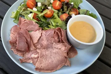 Lengua estofada con su salsa en un recipiente al lado, acompañada de una ensalada variada.