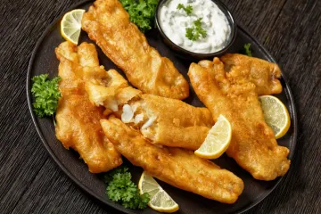 Un plato de pescado rebozado con masa de cerveza y frito, acompañado de salsa tártara.
