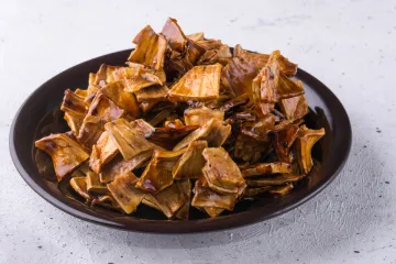 Fruto del pan asado en trozos en un plato oscuro sobre un fondo claro.