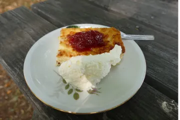 Un trozo de pastel de queso sueco, ostkaka, servido con mermelada de frutos rojos y nata montada.