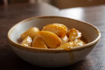 Dientes de ajo caramelizados cubiertos con almíbar dorado en un bol de cerámica sobre una mesa de madera.
