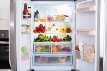 Frigorífico abierto con frutas, verduras, huevos, leche y otros alimentos frescos organizados en estantes y cajones.