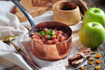 Un cazo de cobre con chutney de manzana rodeado de algunos de sus ingredientes.