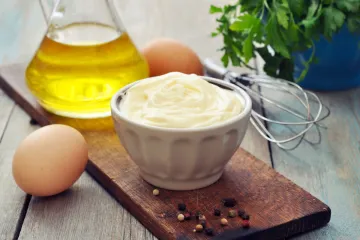 Un cuenco de salsa mayonesa rodeado de los ingredientes y varillas utilizados.