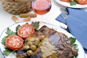 Chuletones de buey con sus guarniciones acompañados de vino tinto.