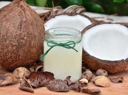 Cocos junto a un recipiente de vidrio con aceite de coco.