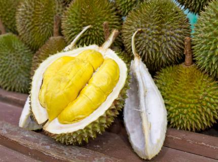 Un durián abierto delante de una pila de frutos maduros.