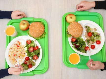 Dos niños con bandejas de comida en el comedor escolar.
