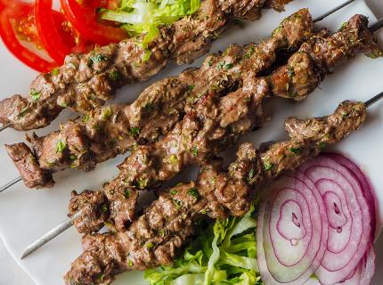 Kebabs de cordero en brochetas de metal acompañados de ensalada.
