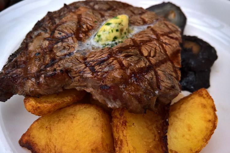 Filete a la plancha con mantequilla aromatizada sobre tabla de madera acompañado de patatas.