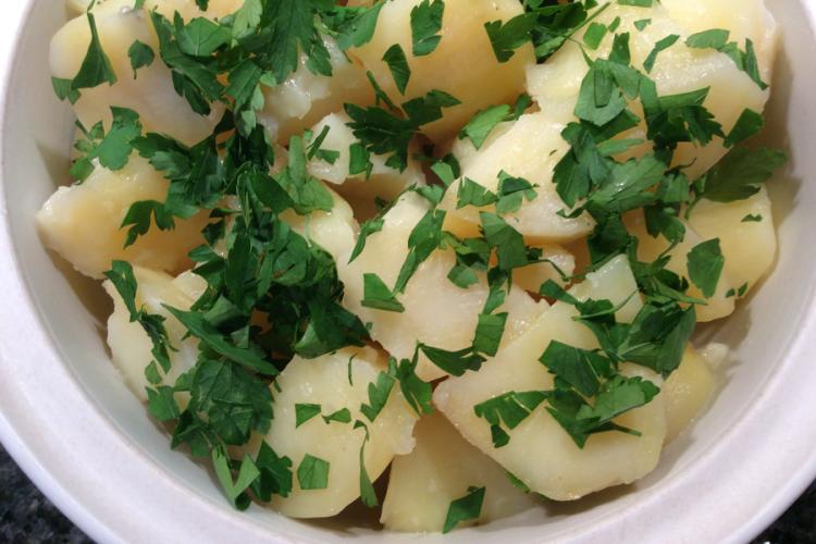 Detalle de patatas hervidas con mantequilla y perejil en una cazuela de loza blanca.