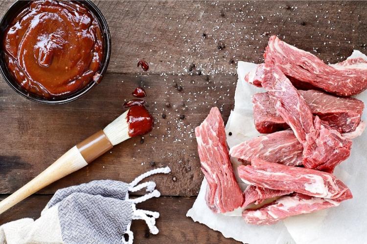 Salsa brbacoa en un cuenco, costillas frescas y un pincel para aplicarla.