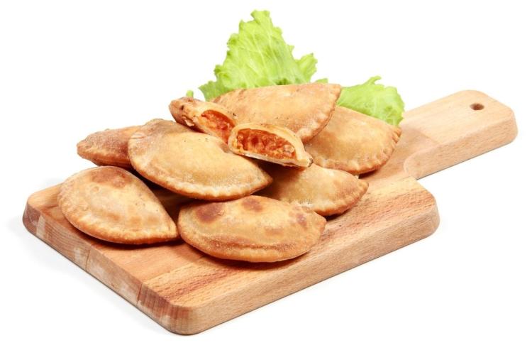 Empanadillas al horno sobre tabla de cortar de madera.