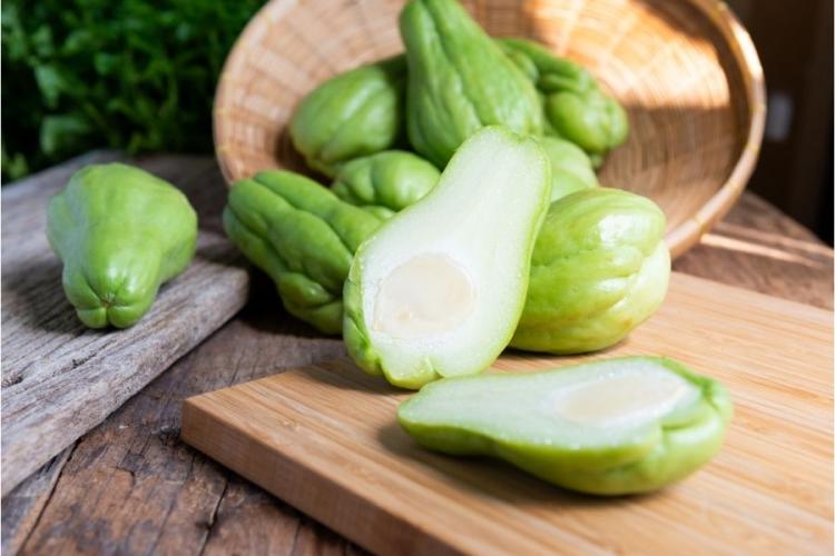 Chayotes frescos enteros y un chayote abierto sobre una tabla de cortar..