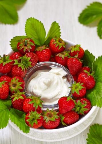 Un cuenco de crema de queso a la vainilla rodeado de fresas frescas.