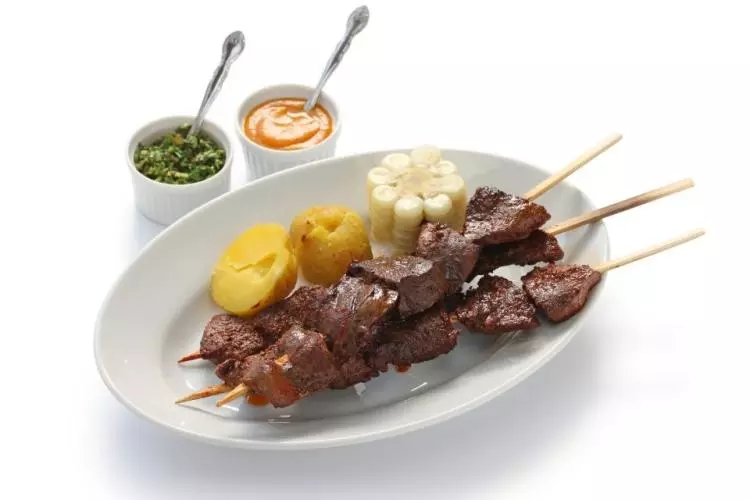 Anticuchos de corazón con patata cocida, choclo y salsas.
