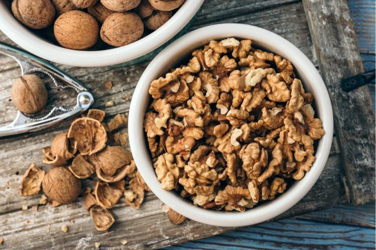 Un cuenco de nueces peladas con un cascanueces y un cuenco con nueces enteras al lado.