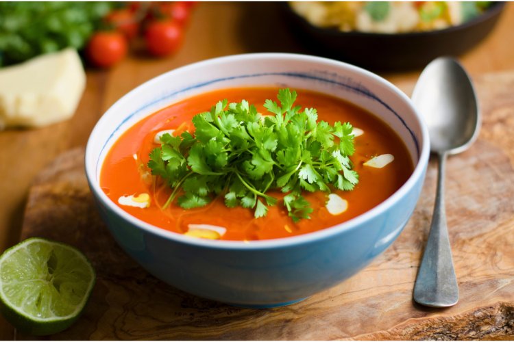 Un cuenco con sopa de jitomate decorada con nata líquida, aceite de oliva y cilantro fresco.