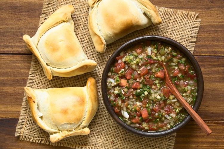 Salsa pebre con tomate en un cuenco con tres empanadas chilenas alrededor.