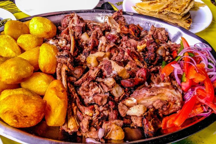 Nyama choma con patatas y una ensalada kumburi de tomate y cebolla morada.