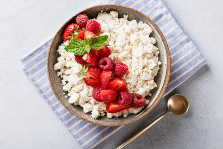 Un cuenco de requesón casero con fresas y frambuesas, decorado con hierbabuena.