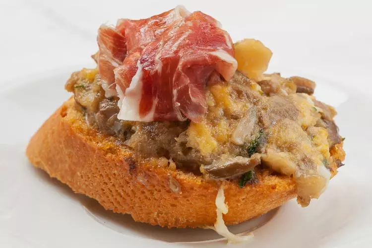 Pincho de revuelto de setas decorado con una loncha de jamón serrano.