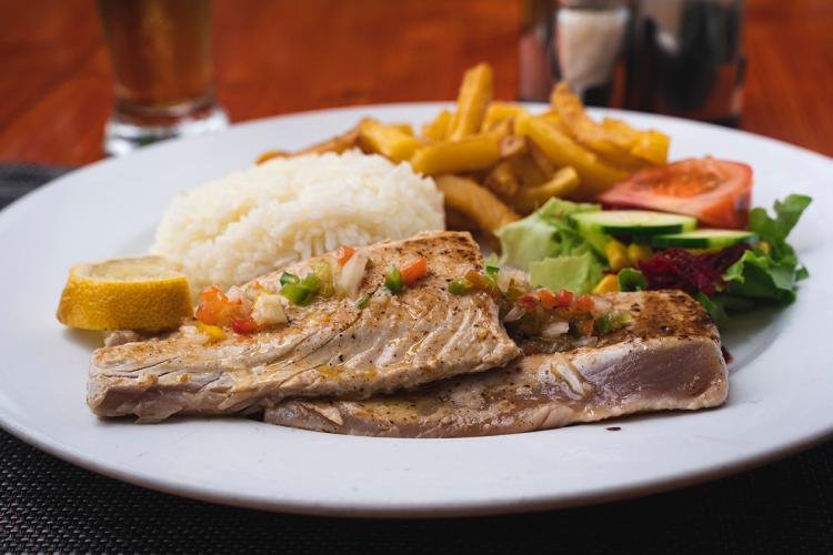 Atún a la parrilla servido con arroz, patatas fritas y ensalada.