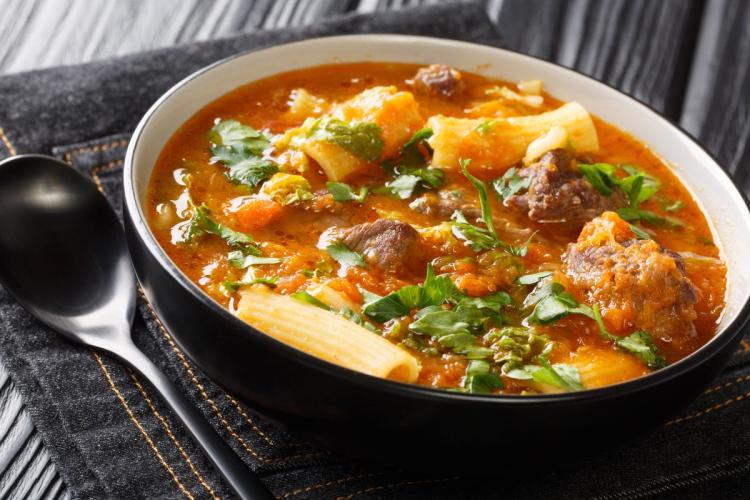 Un plato hondo de sopa joumou haitiana, con ternera, pasta y verduras en un caldo espeso, decorada con hojas de perejil fresco. 