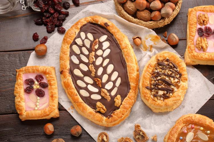 Varios pasteles polacos mazurek decorados con chocolate, nueces y frutas secas, colocados sobre una superficie rústica de madera con avellanas y arándanos secos.