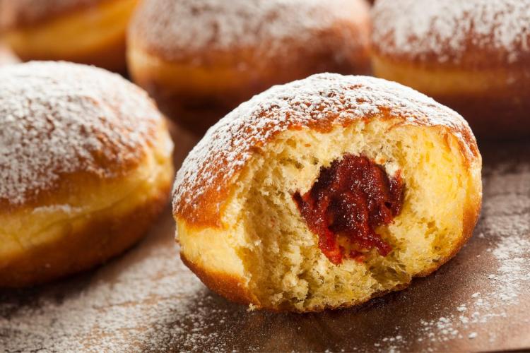 Primer plano de paczki, donuts polacos rellenos de jalea, con uno mostrando el relleno rojo al haber sido mordido y espolvoreados con azúcar en polvo.